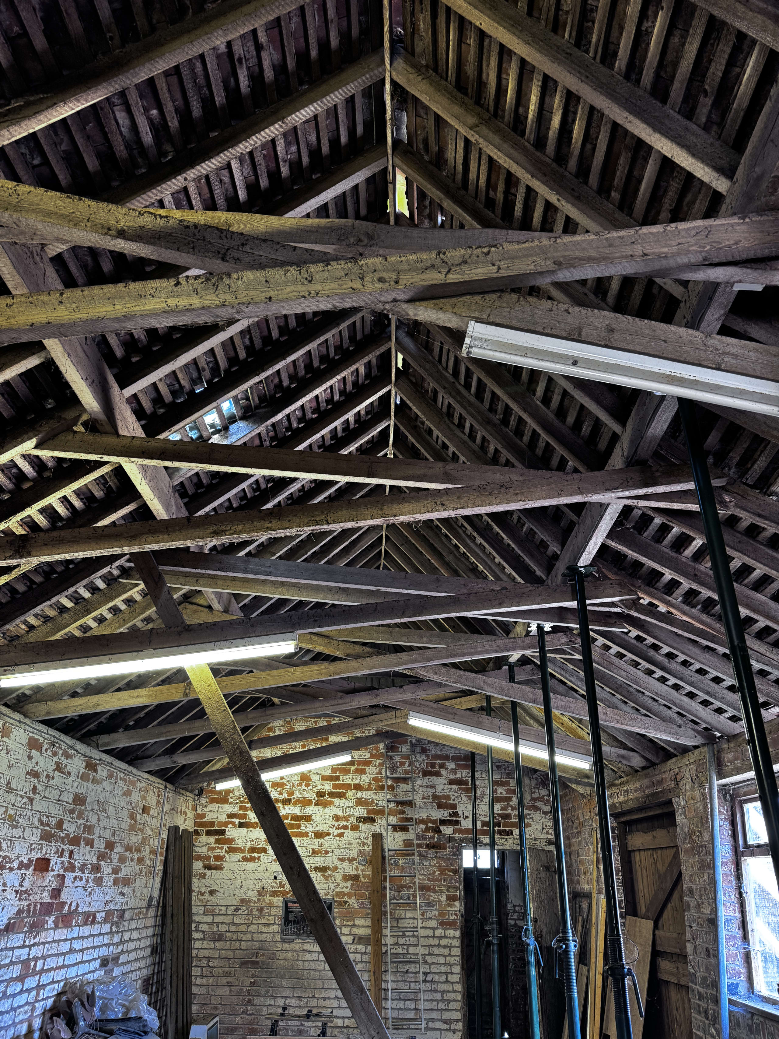 Interior view of historic timber roof truss structure with exposed wooden beams and battens above weathered brick walls