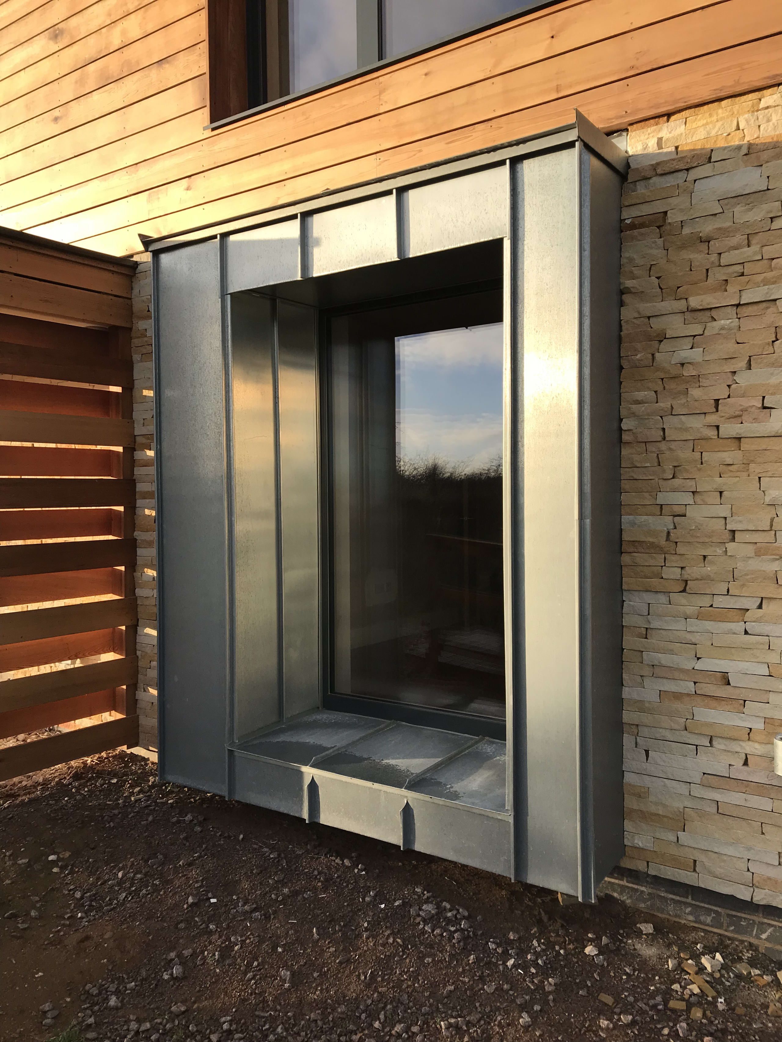Zinc-clad window bay projecting from a timber and stone-tiled house facade