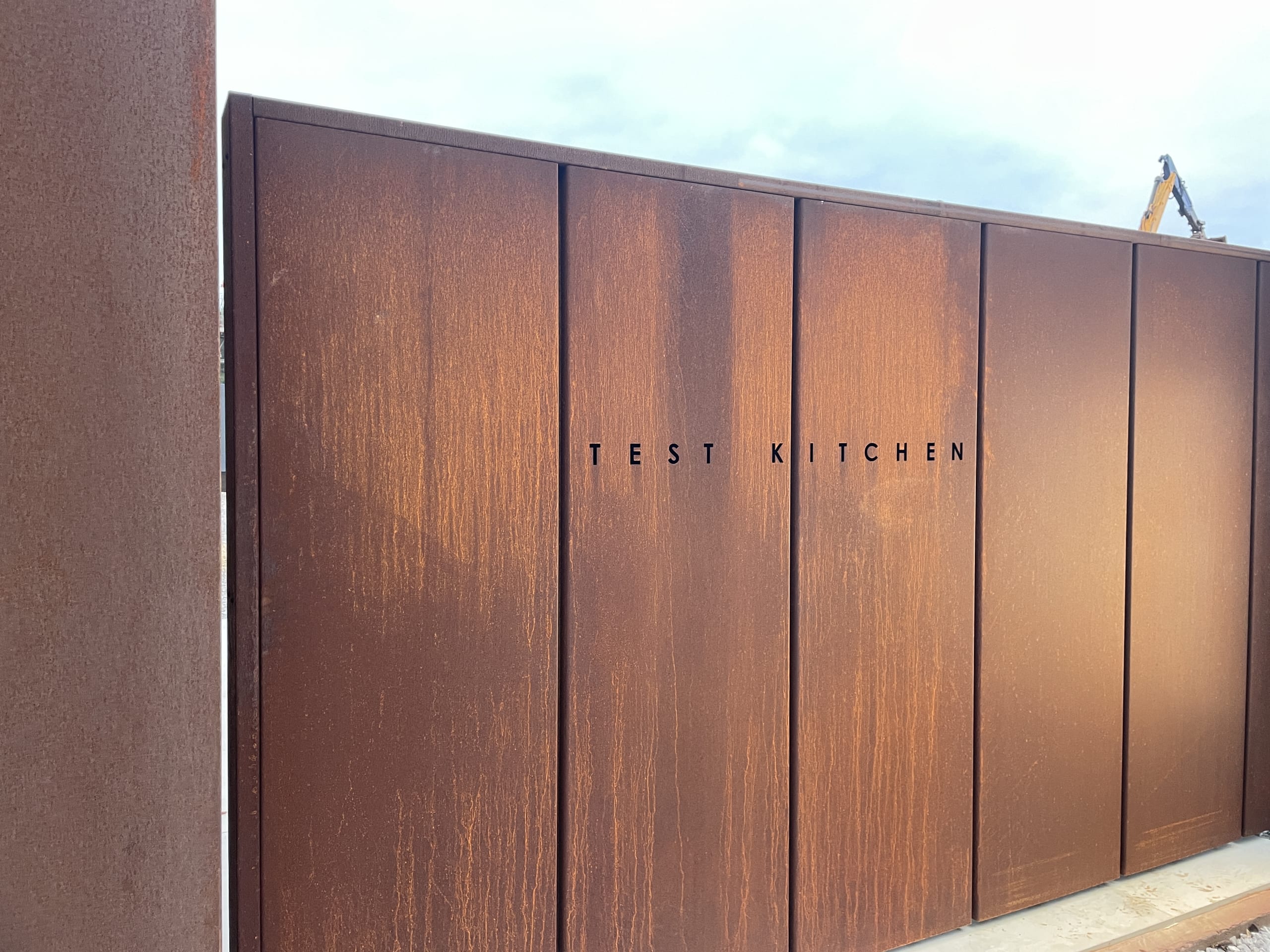 Corten steel exterior wall with minimalist TEST KITCHEN signage in black lettering against weathered rust patina