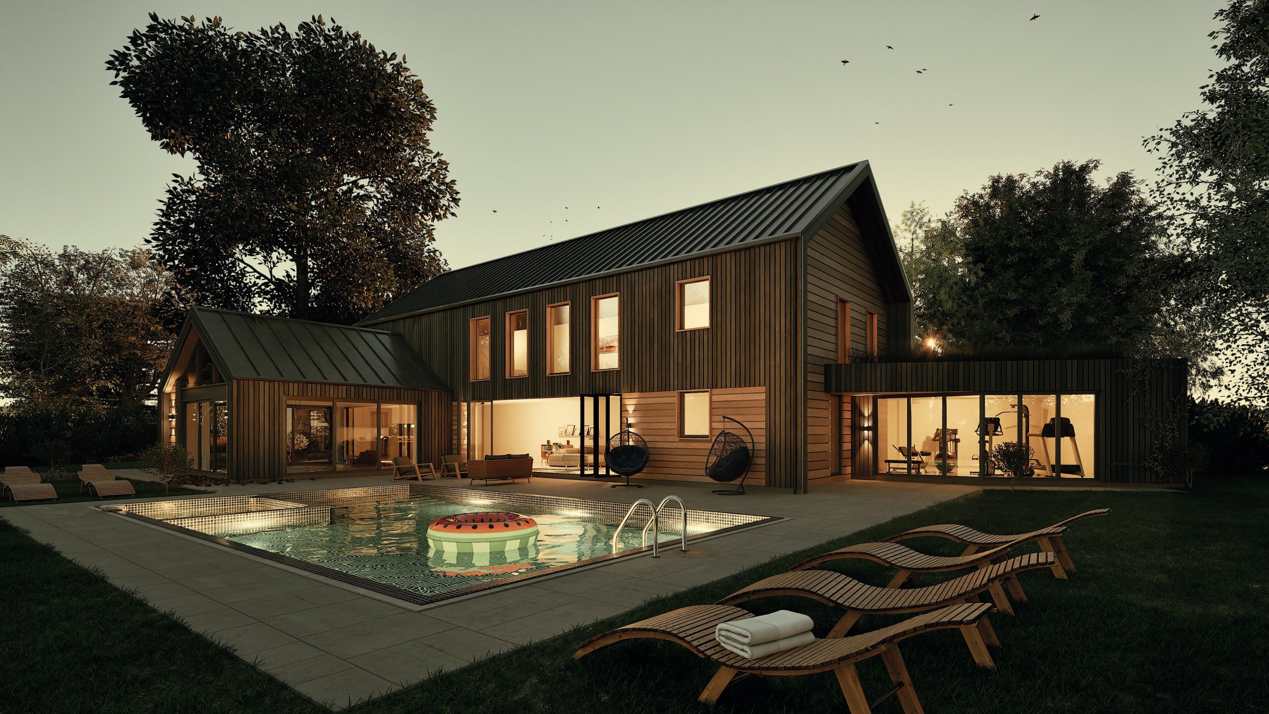 Modern dark timber barnhouse with metal roof, illuminated windows, outdoor pool with watermelon float, and wooden loungers at dusk