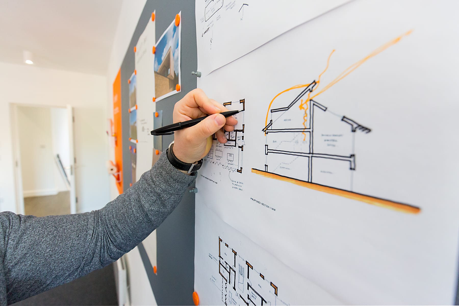 Hand holding a pen annotates a pinned-up architectural section drawing with orange highlight marks