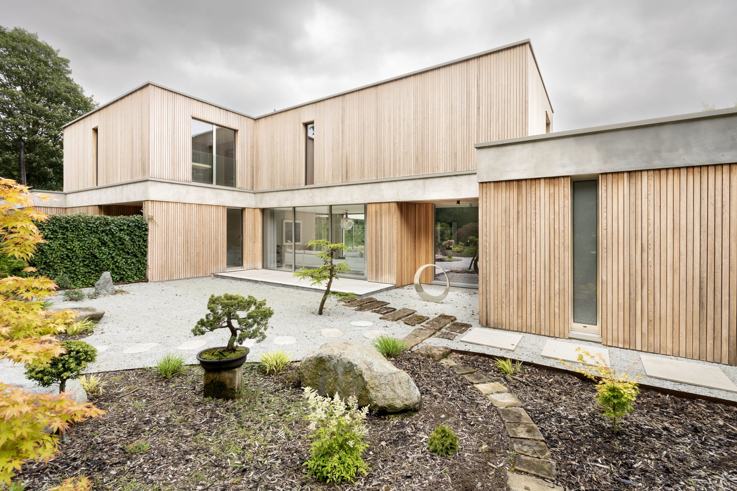 Timber-clad two-story home wraps around a Japanese-style gravel garden with bonsai and boulders