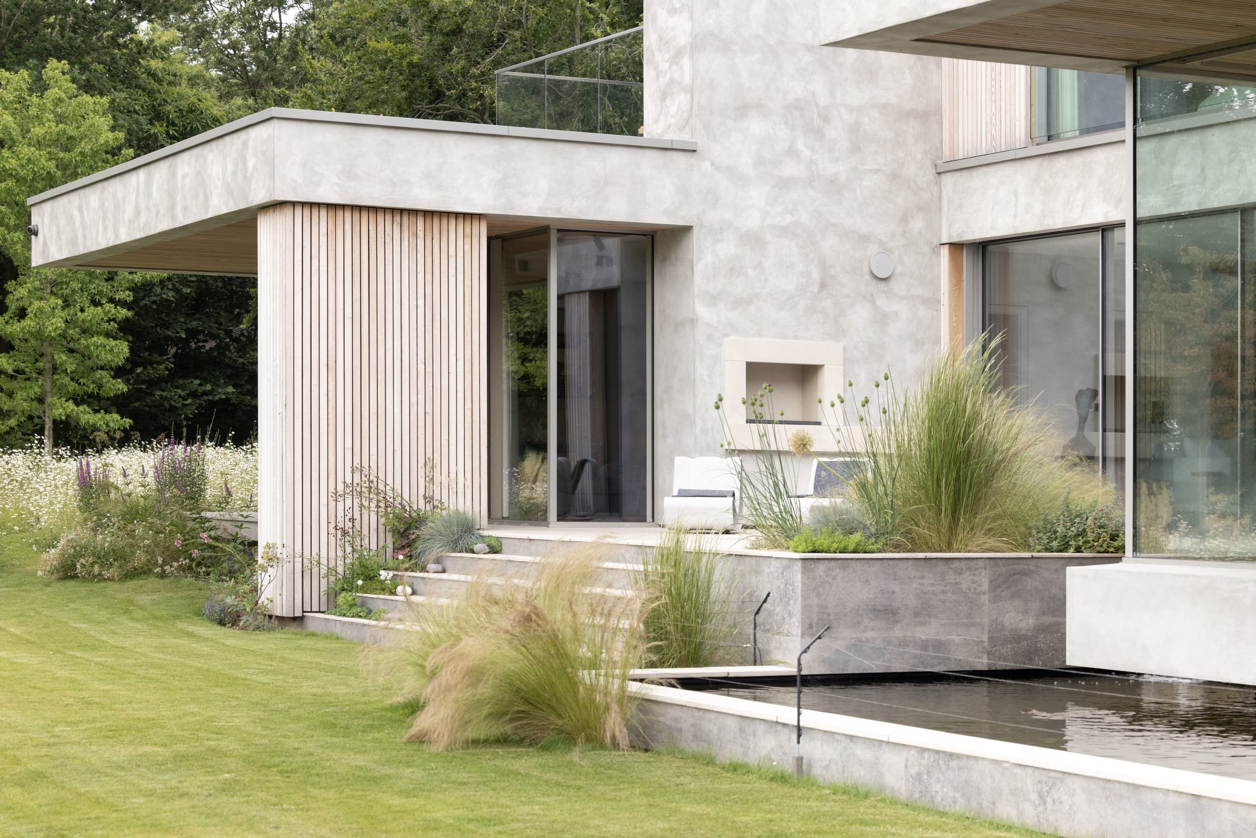 Contemporary house with timber-clad extension, render walls, and a reflecting pool bordered by ornamental grasses