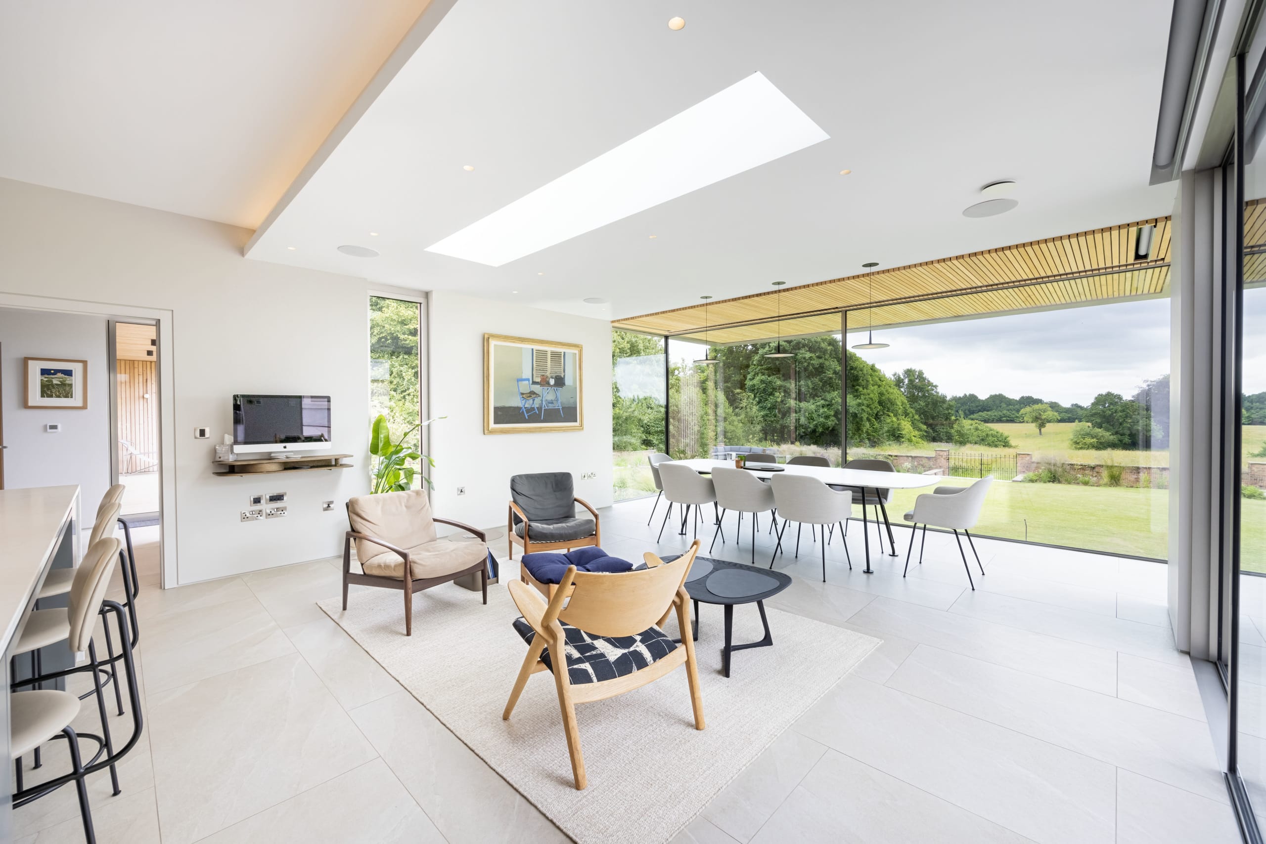 Open-plan living and dining area with wood-slat ceiling detail and full-height glass doors opening to countryside views