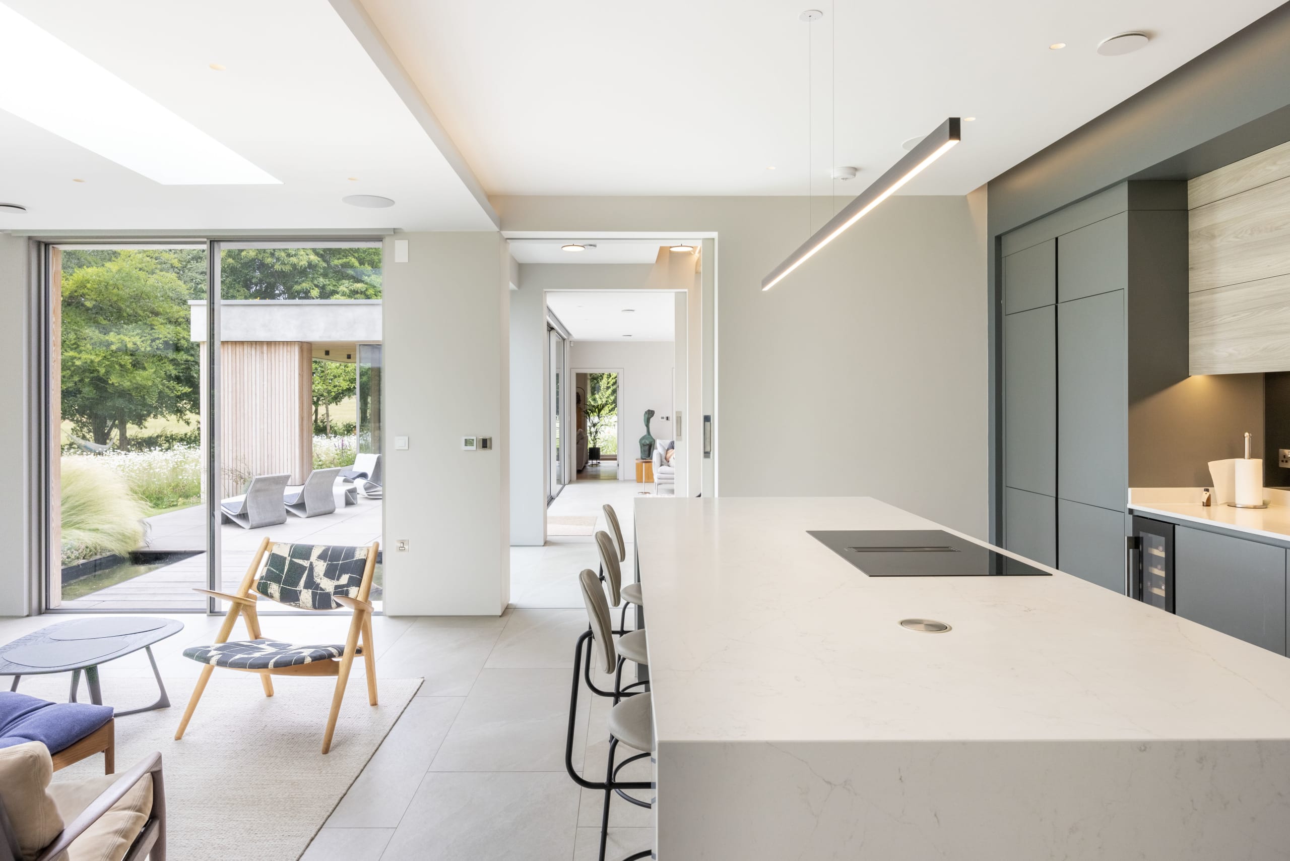 Open-plan kitchen with marble island and matte cabinetry opens to living area and garden beyond