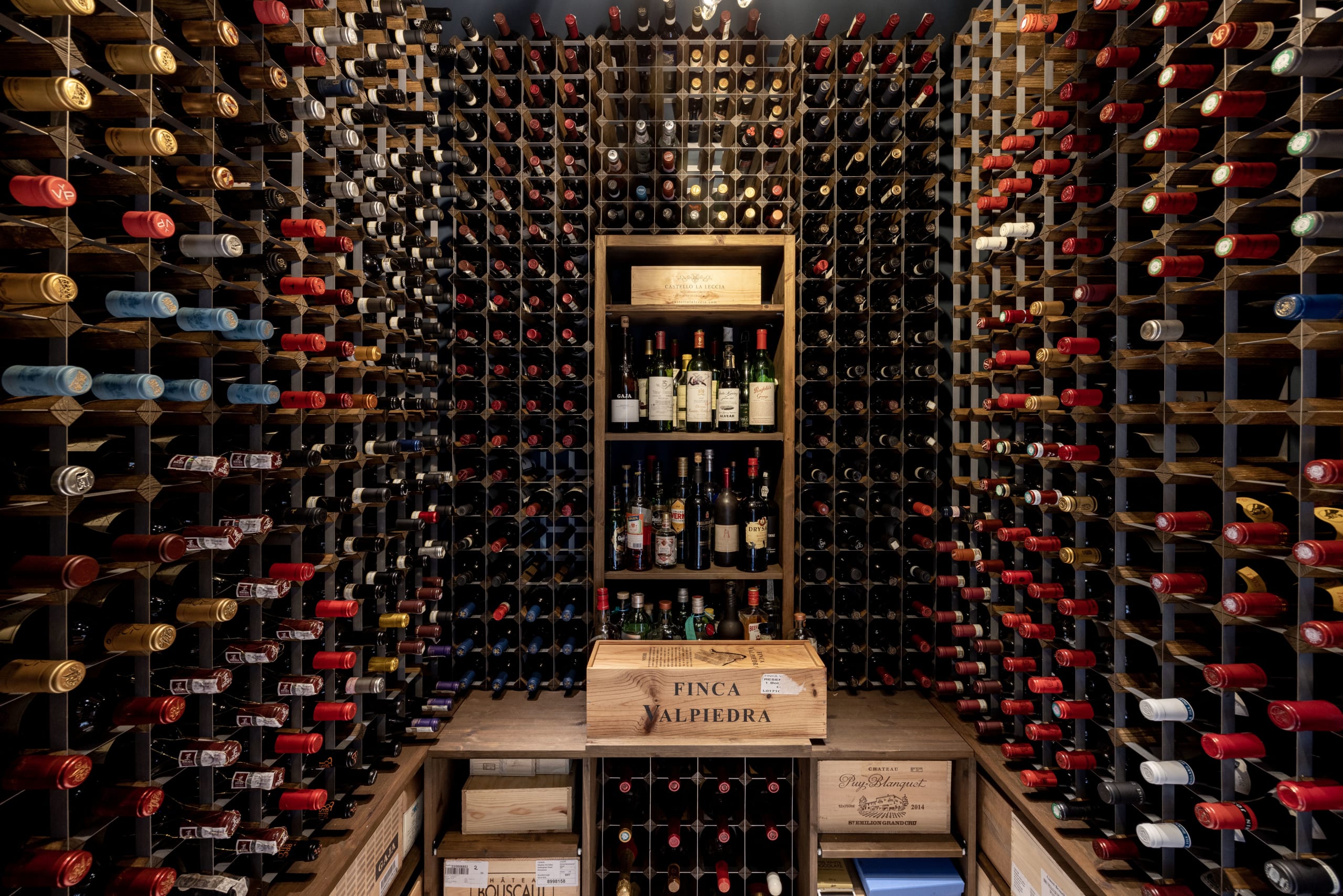Wine cellar with wood-and-metal diamond racks filled with bottles surrounding a central display shelf