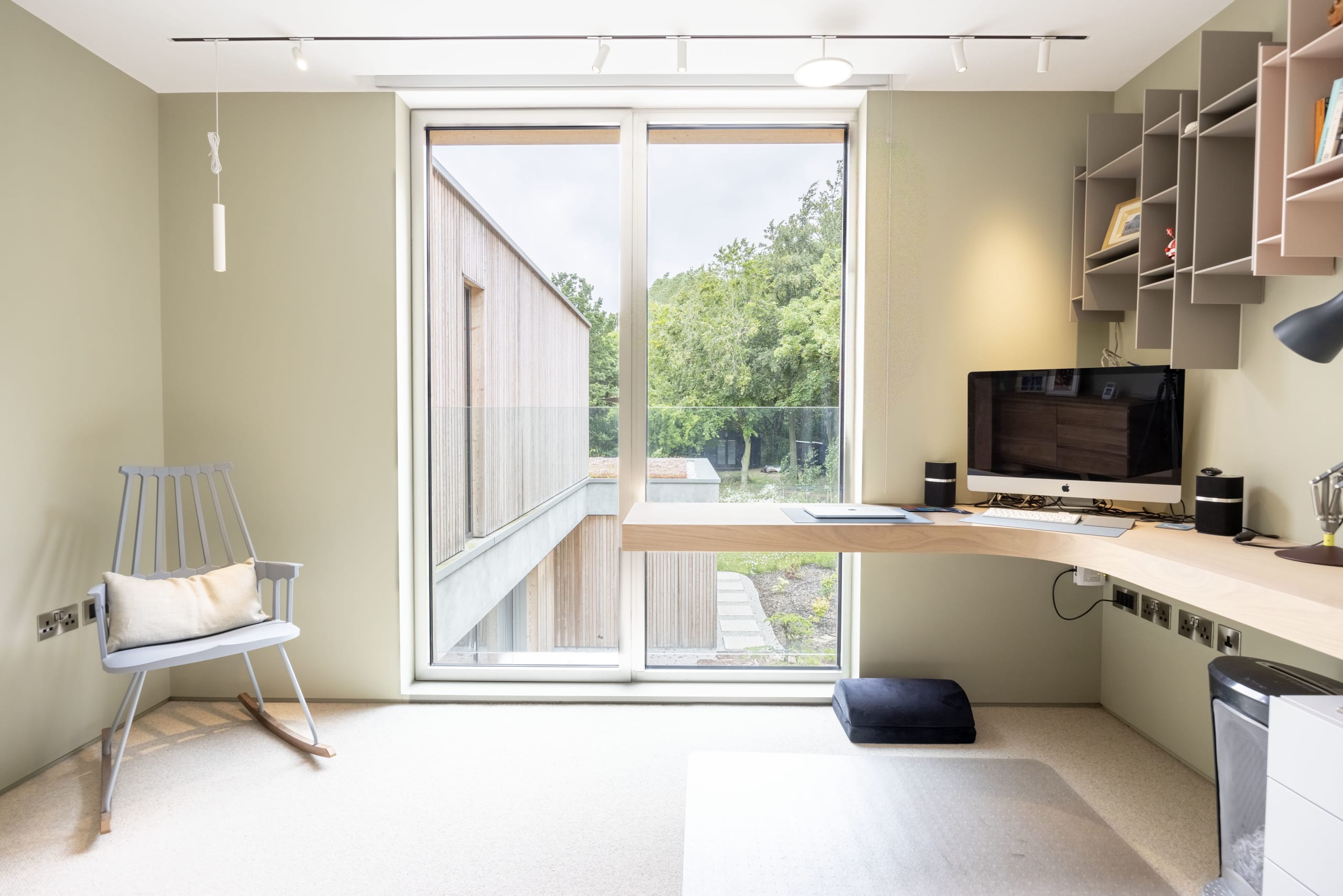 Home office with built-in wood desk, angled asymmetric shelving, and a large window overlooking a timber-clad extension