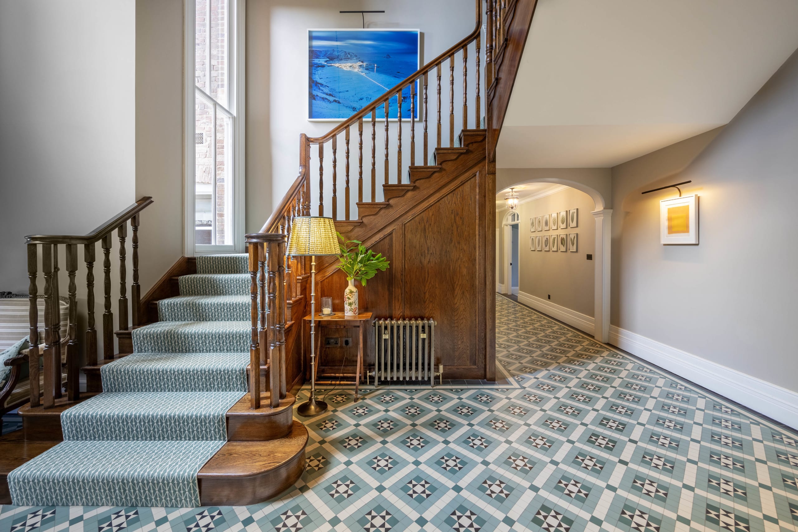 Entry hall with dark wood staircase, patterned stair runner, and geometric tile floor leading to an arched corridor