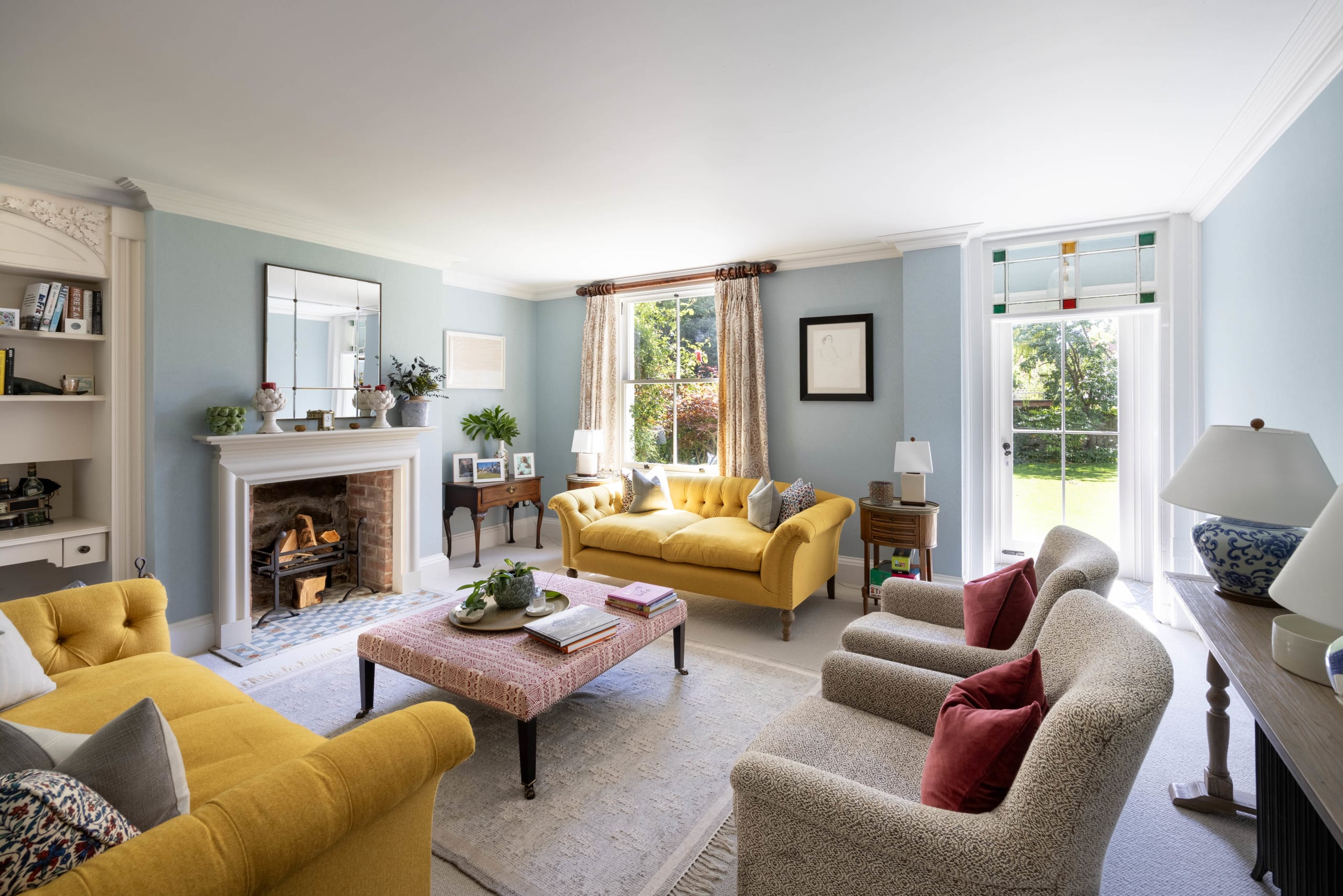 Traditional living room with pale blue walls, yellow velvet sofas, and a period fireplace with brick surround