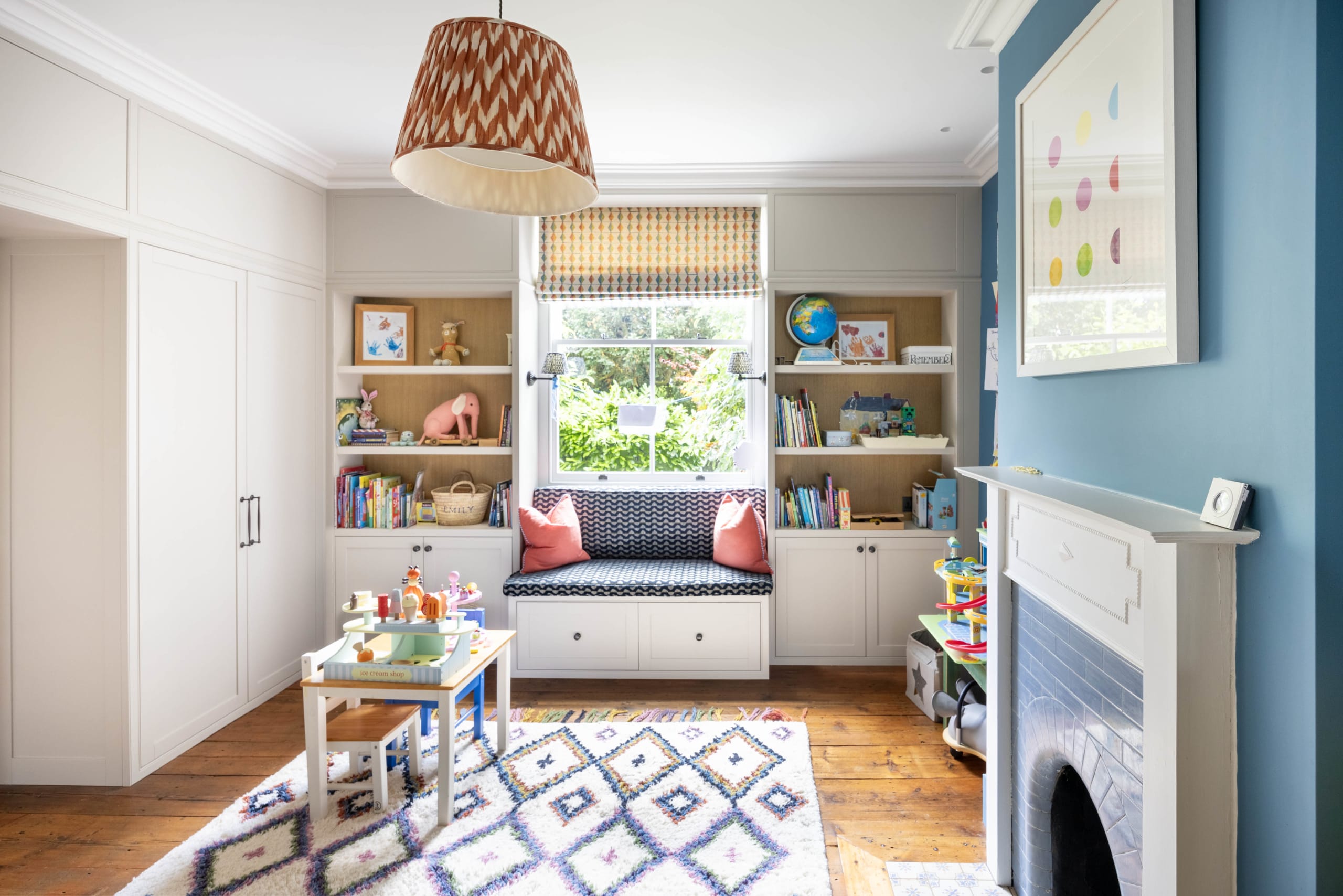 Children's playroom with built-in window seat, bookshelves, and blue accent wall with fireplace