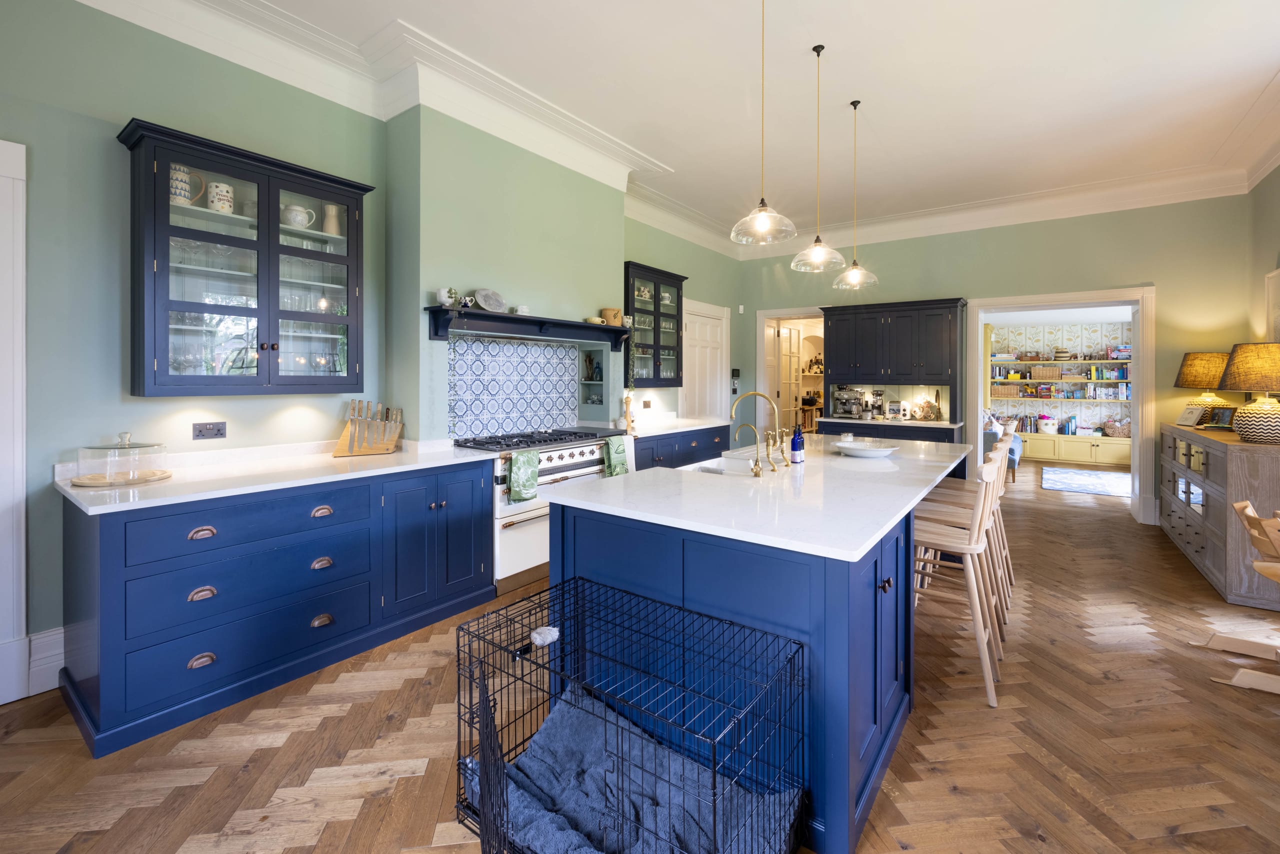 Navy blue kitchen with white countertops, herringbone wood flooring, and glazed display cabinets