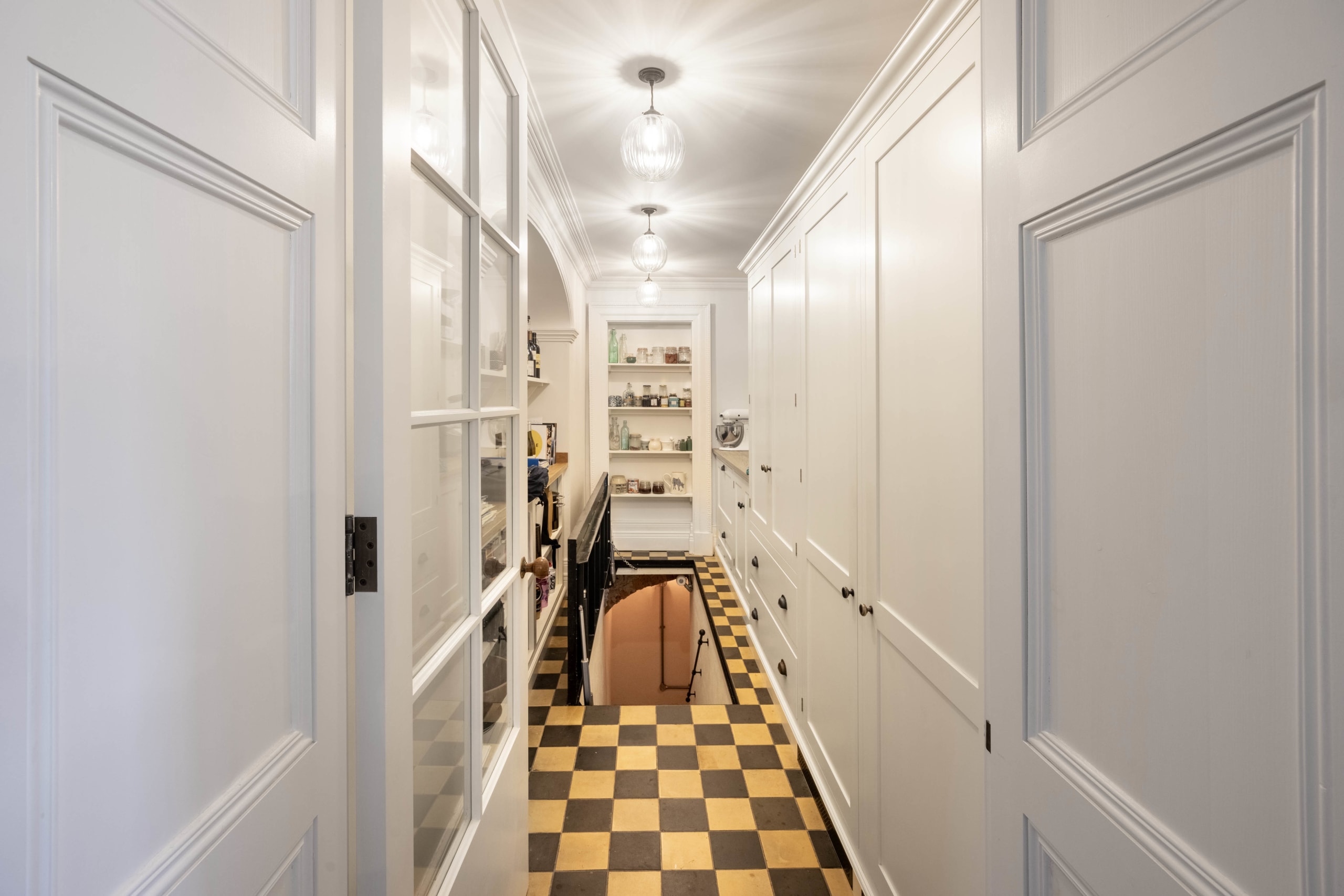 Narrow butler's pantry hallway with white paneled cabinetry and a checkerboard tile floor