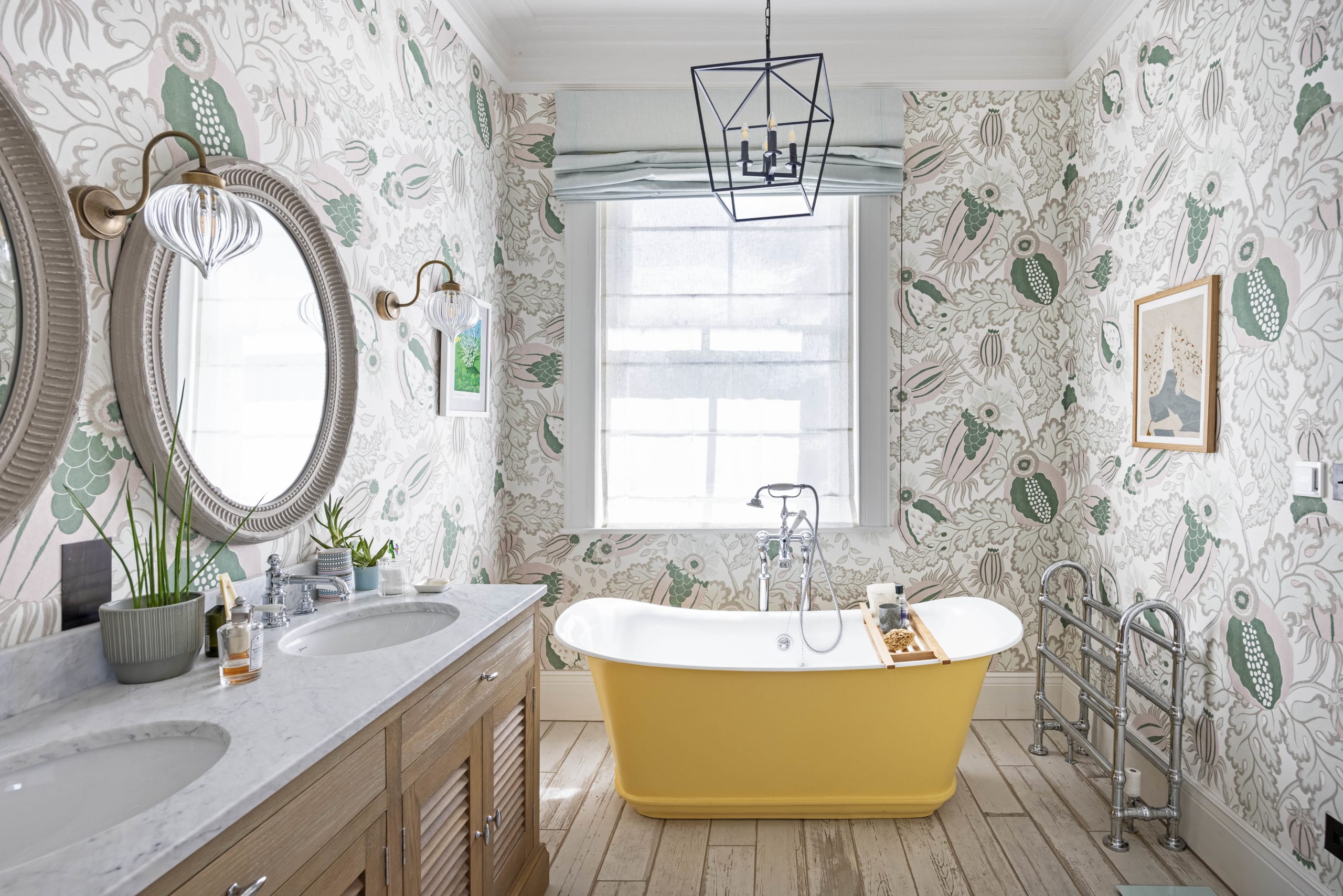 Elegant bathroom with yellow freestanding tub, botanical wallpaper, wood vanity with marble top, and geometric pendant light
