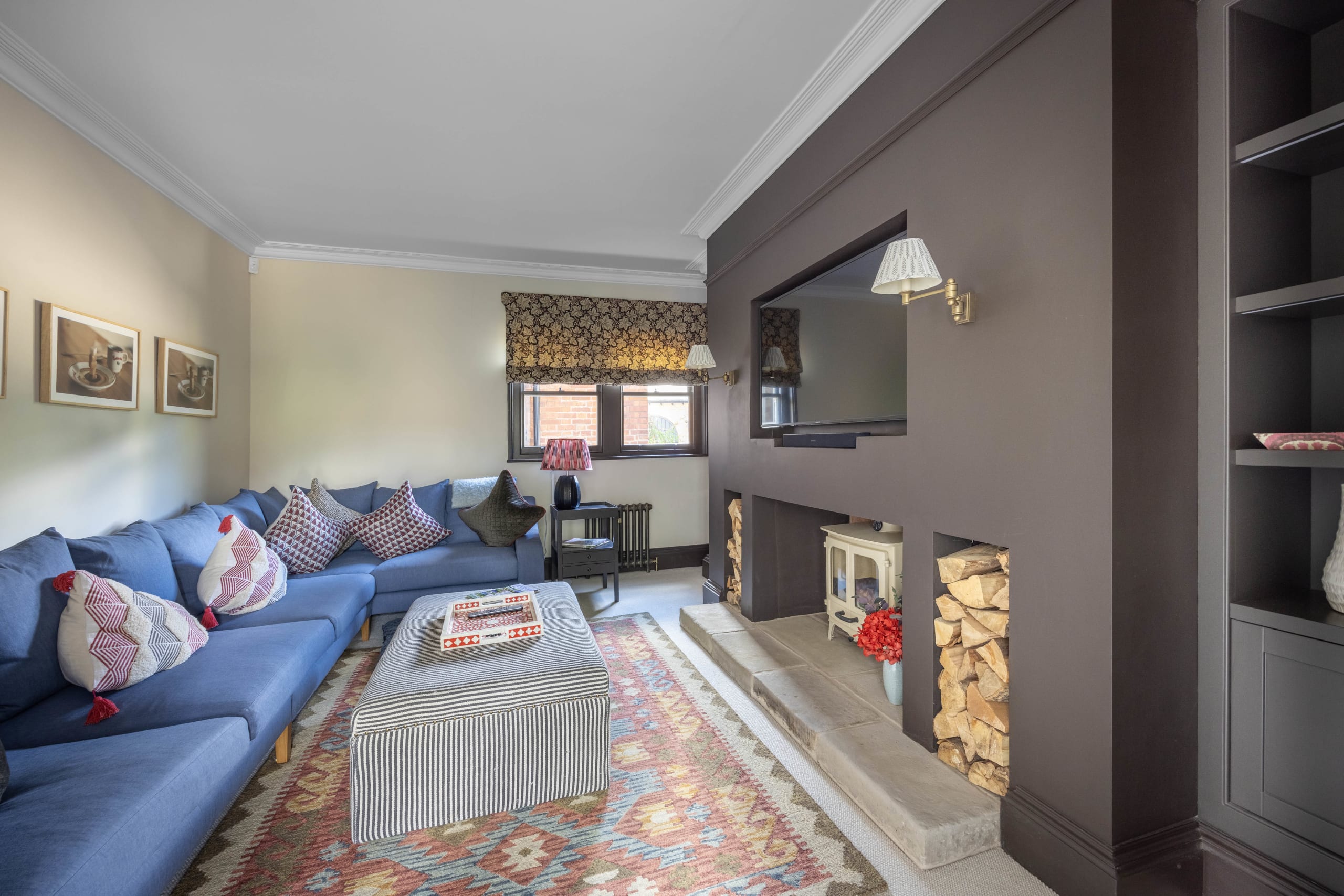 Modern living room with blue L-shaped sofa, wood-burning stove, built-in dark grey shelving, and colorful kilim rug