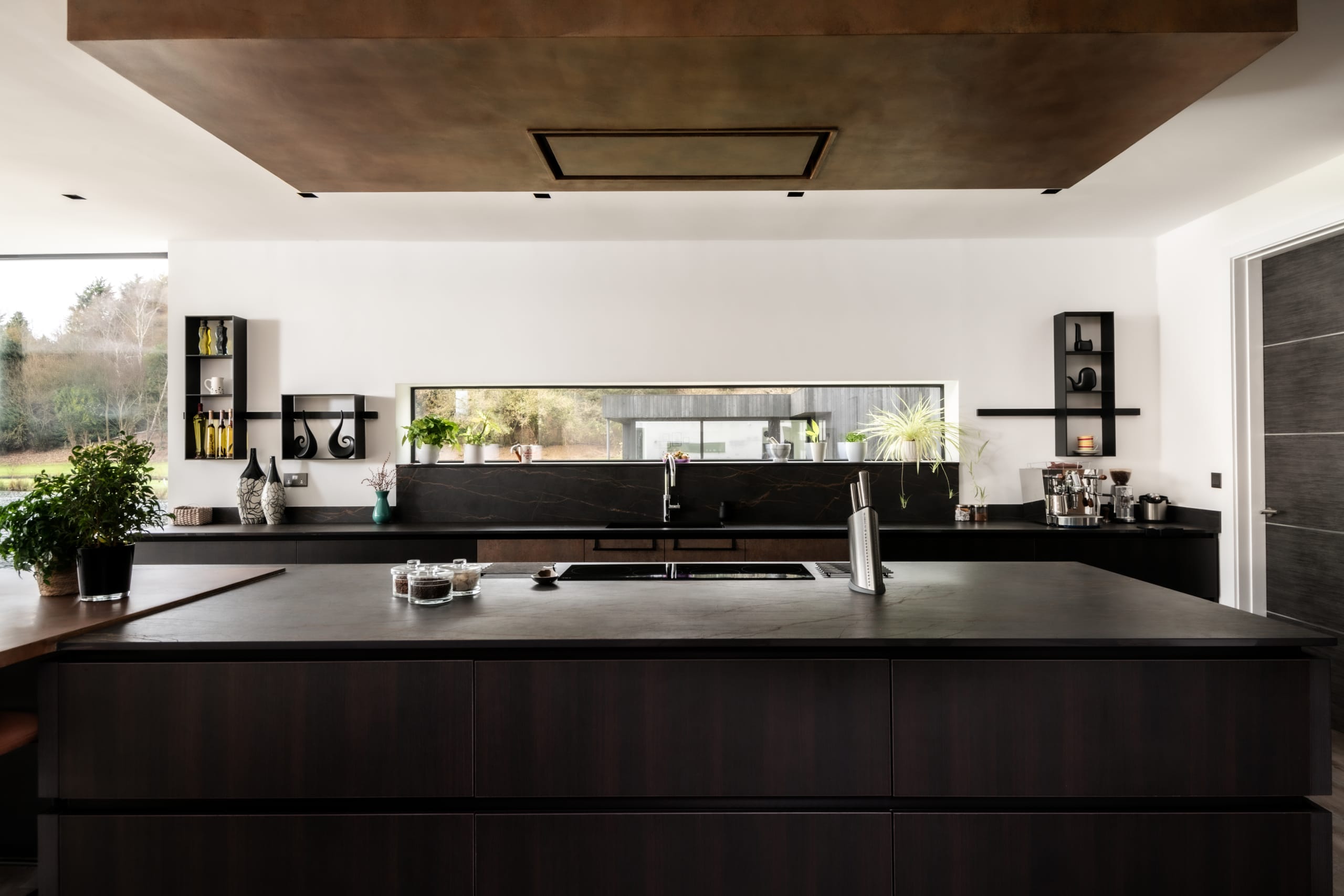 Modern luxury kitchen with dark wood island, black marble backsplash, bronze ceiling feature, and horizontal window