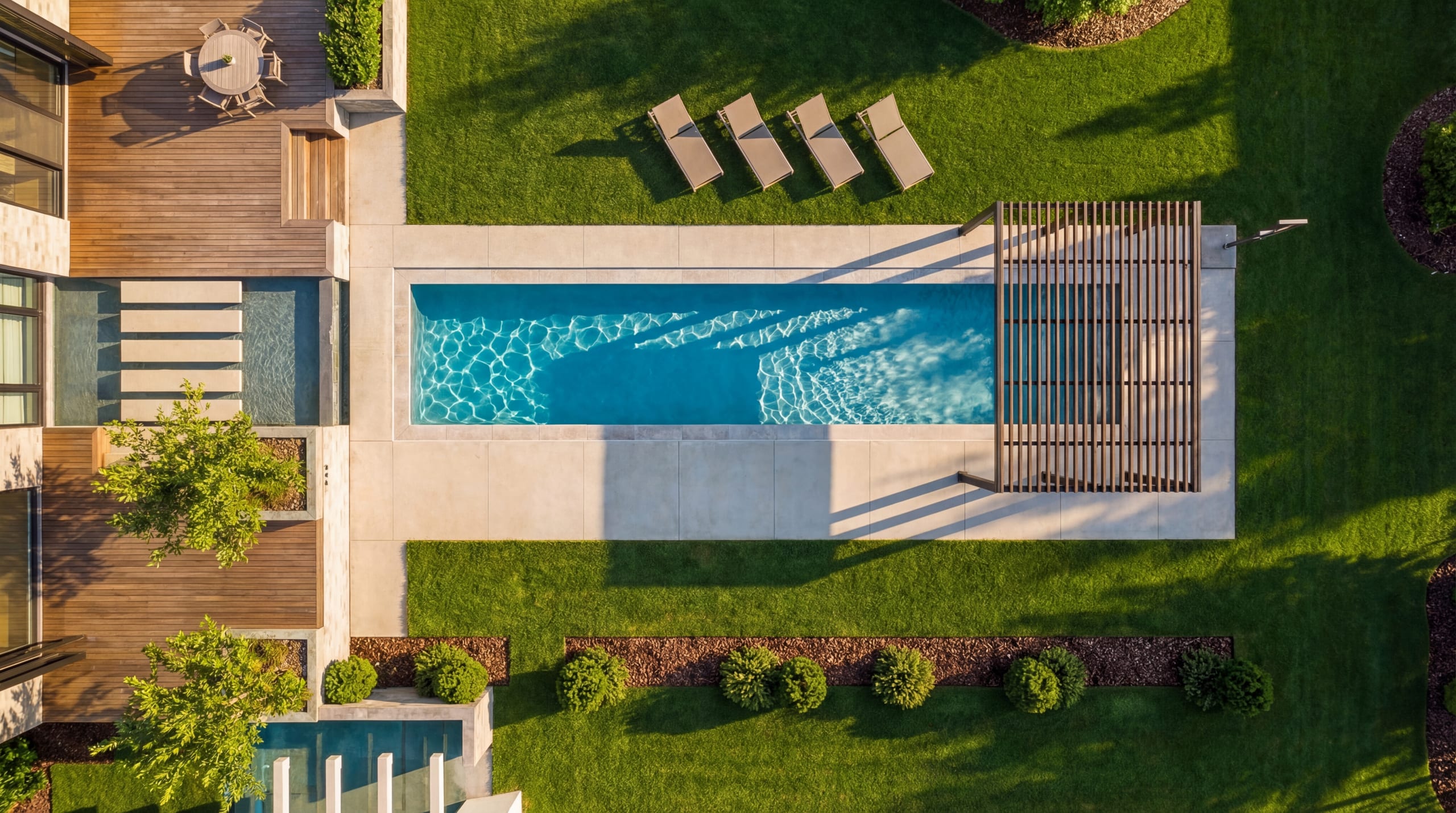 Aerial view of a rectangular backyard pool with wood slat privacy screen, stone decking, and manicured lawn