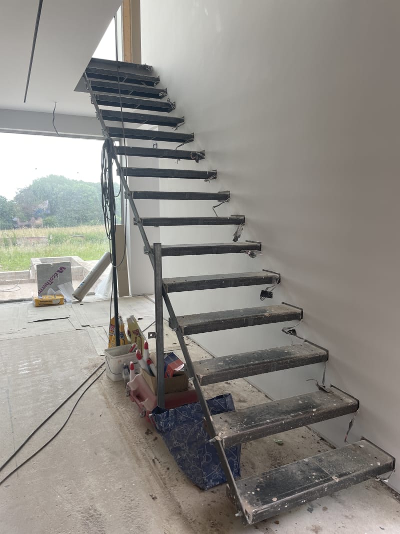 Modern floating steel staircase under construction with cantilevered treads mounted to wall, temporary support in place
