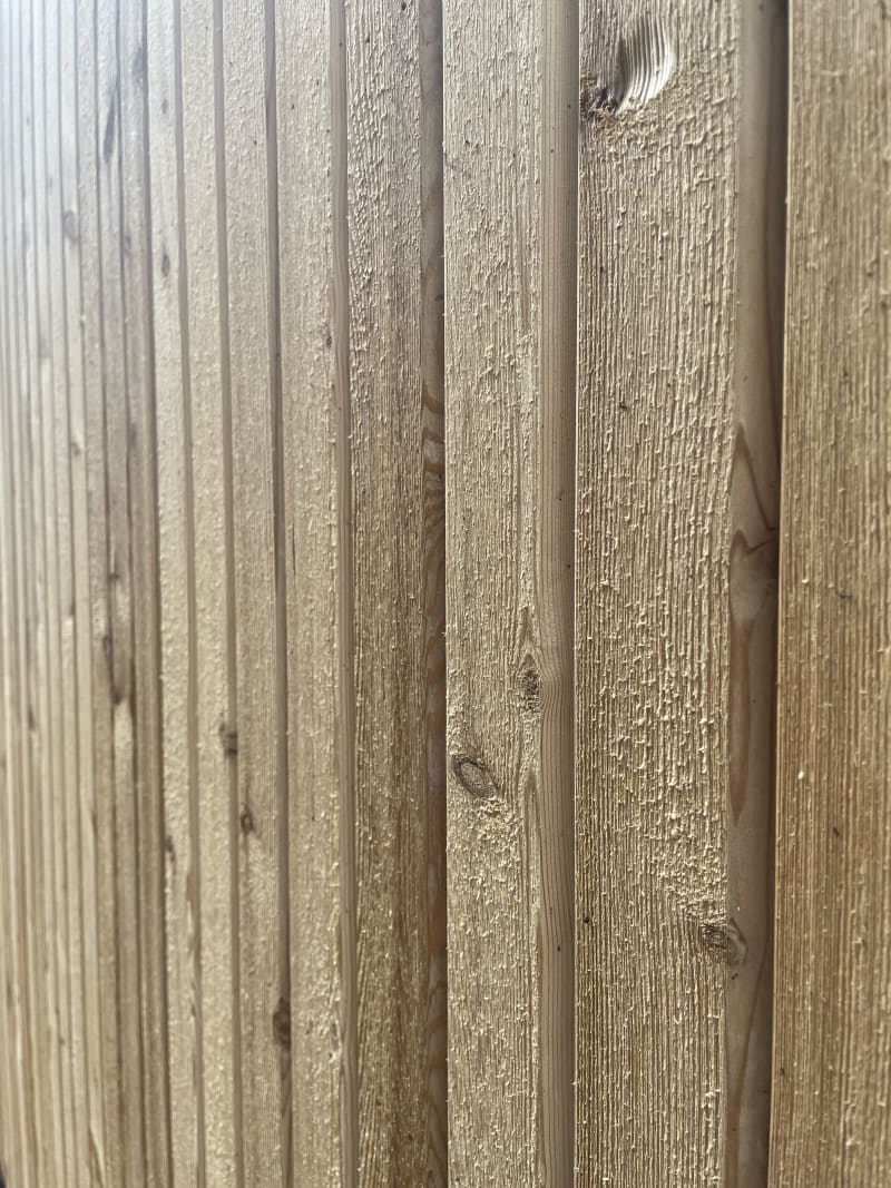 Close-up of vertical wooden cladding panels showing natural grain texture and knots in light tan pine timber