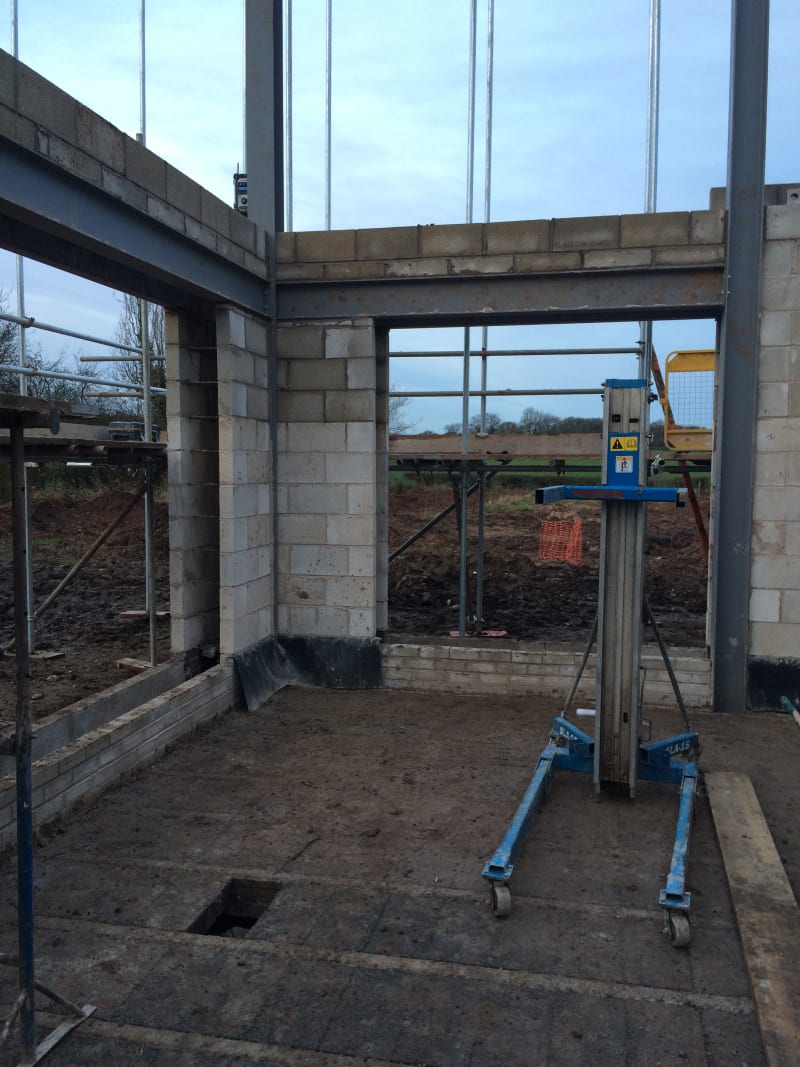 Construction site showing concrete block walls, steel frame structure, scaffolding, and material lift on concrete slab foundation