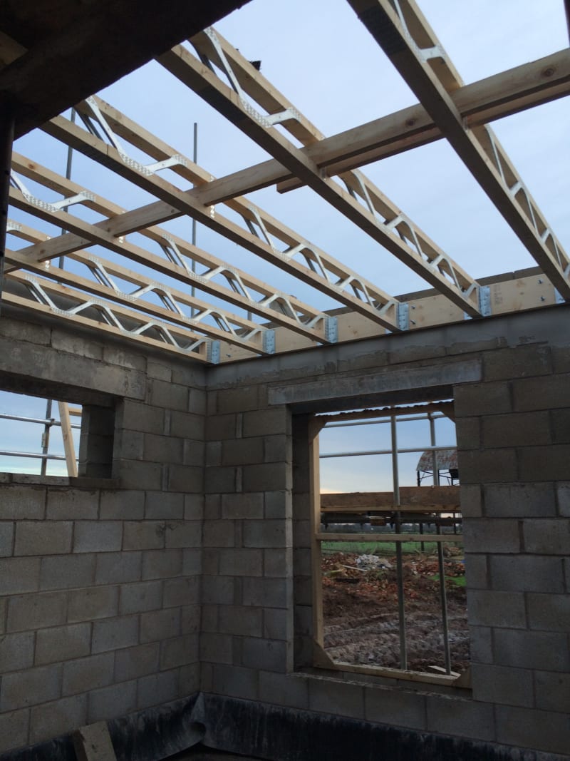 Residential construction site showing concrete block walls with wooden roof trusses and metal joist hangers being installed