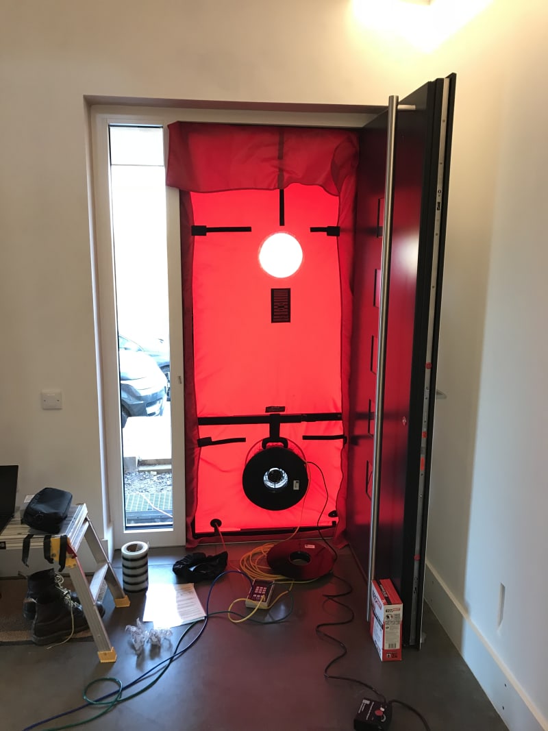 Red blower door fan sealed into an entrance doorway during an airtightness test on a construction site
