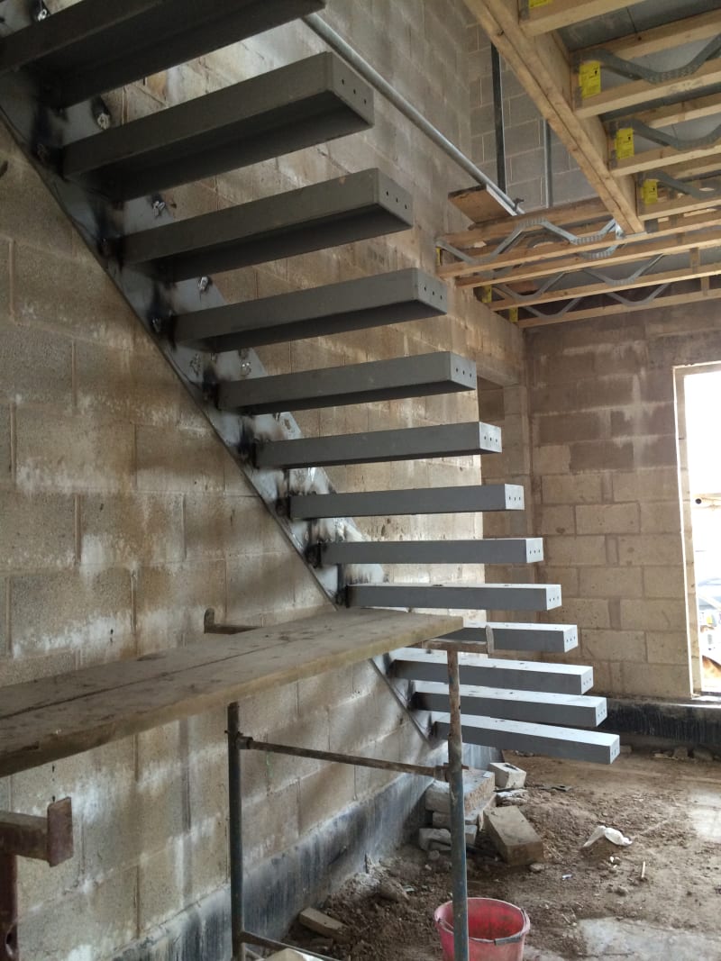 Floating cantilever steel staircase with rectangular treads anchored to concrete block wall during construction phase