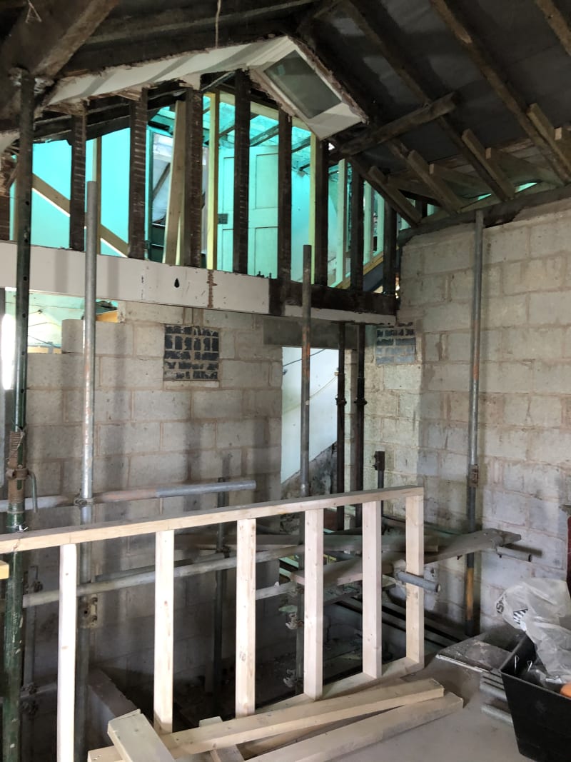 Building interior mid-renovation with exposed steel props, timber studwork, and blockwork walls beneath open roof rafters