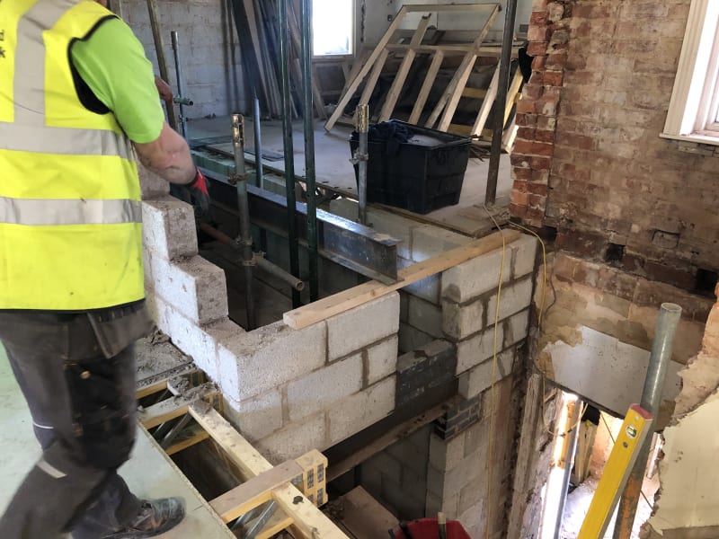 Worker in hi-vis vest building a blockwork wall on a steel lintel during a structural renovation