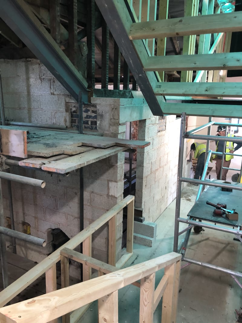 Construction site interior showing exposed steel beams, blockwork walls, timber framing, and scaffolding
