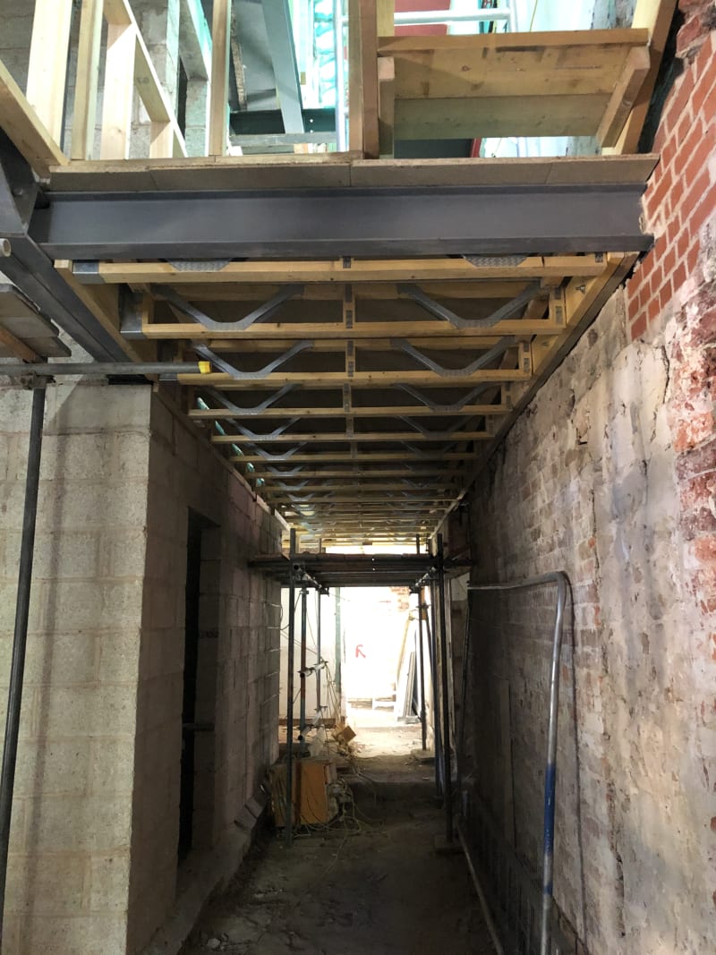 Steel beam and timber joist floor structure spanning a narrow construction corridor between brick and block walls