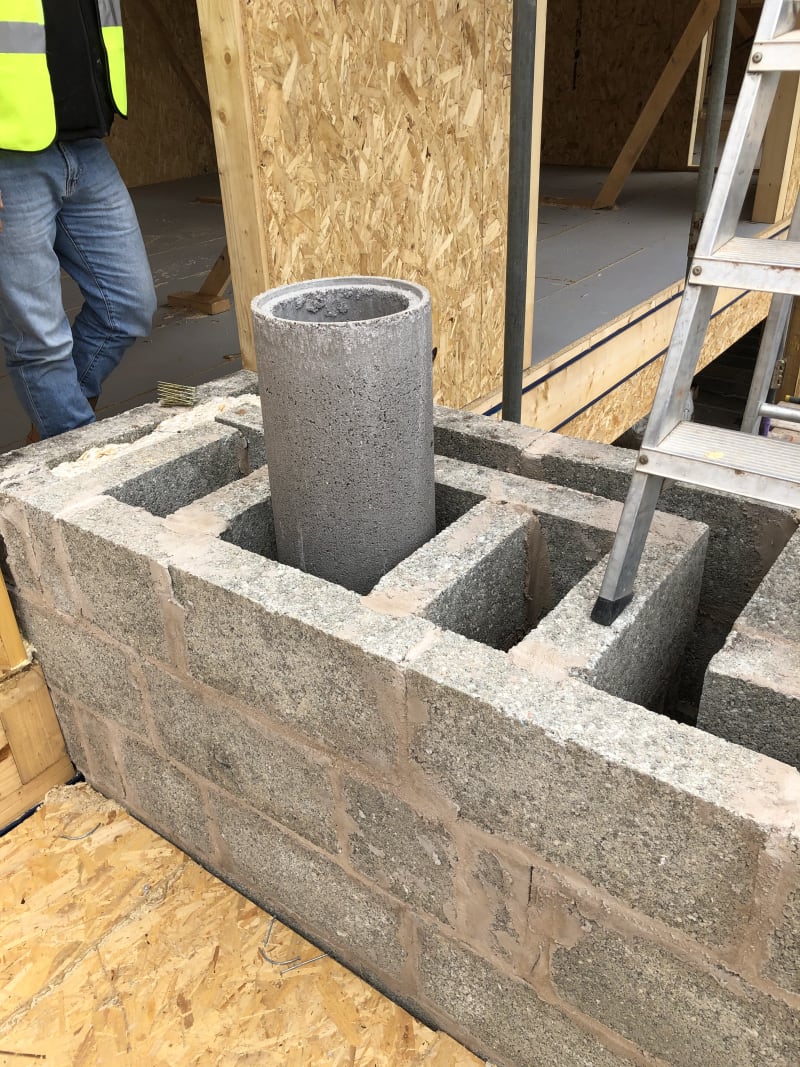 Concrete flue liner set into a blockwork chimney stack under construction, with OSB-clad framing behind