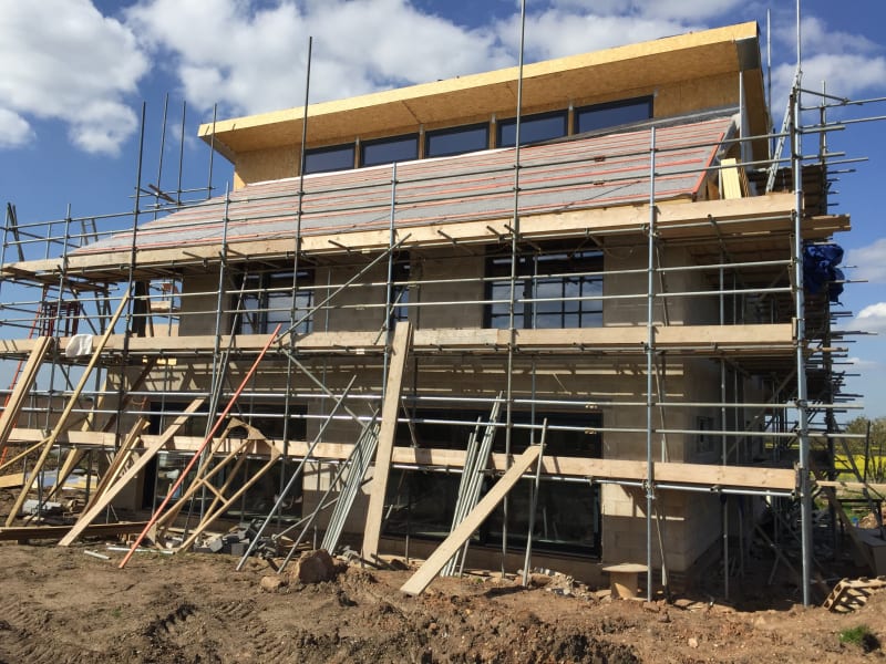 Modern two-story residential building under construction with scaffolding, large windows, and partially completed roof