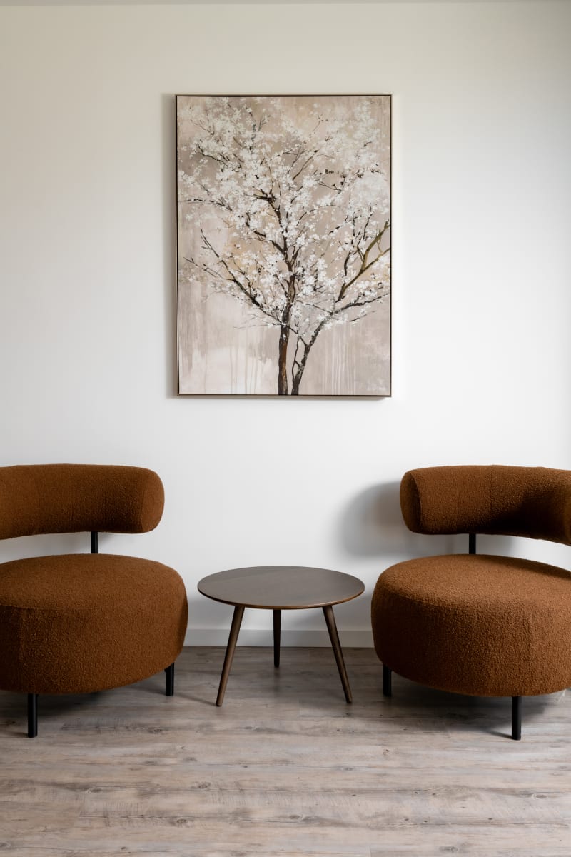 Modern seating area with two rust-colored bouclé curved chairs, small round wooden table, and cherry blossom artwork
