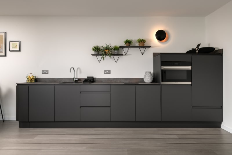 Modern minimalist kitchen with dark grey handleless cabinets, concrete-effect countertops, built-in appliances, and floating shelves