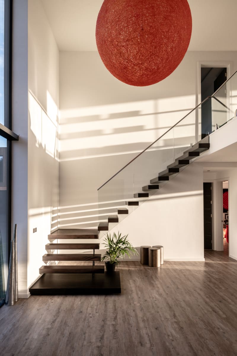 Modern floating staircase with dark wood treads, glass railing, and large red spherical pendant light in double-height foyer