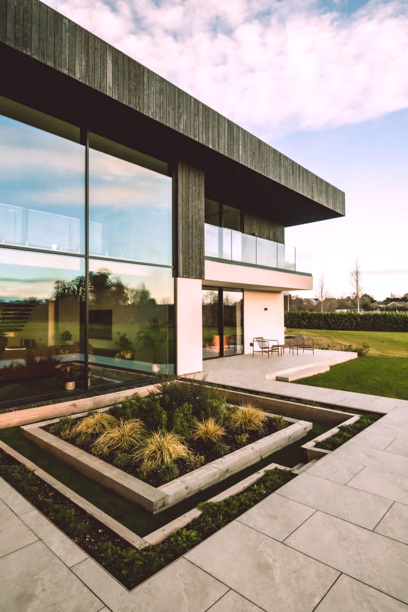 Modern two-story home with dark timber cladding, floor-to-ceiling windows, and geometric sunken garden with ornamental grasses