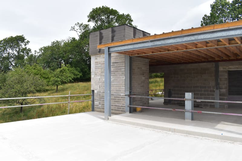 Agricultural building under construction with concrete block walls, steel beams, timber roof framing, and fresh concrete slab