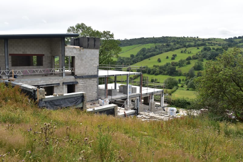 Modern residential construction in progress with concrete block walls and steel frame terrace overlooking green rolling hills