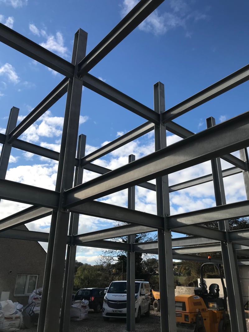 Steel frame structure under construction with exposed beams and columns against blue sky, construction vehicles below