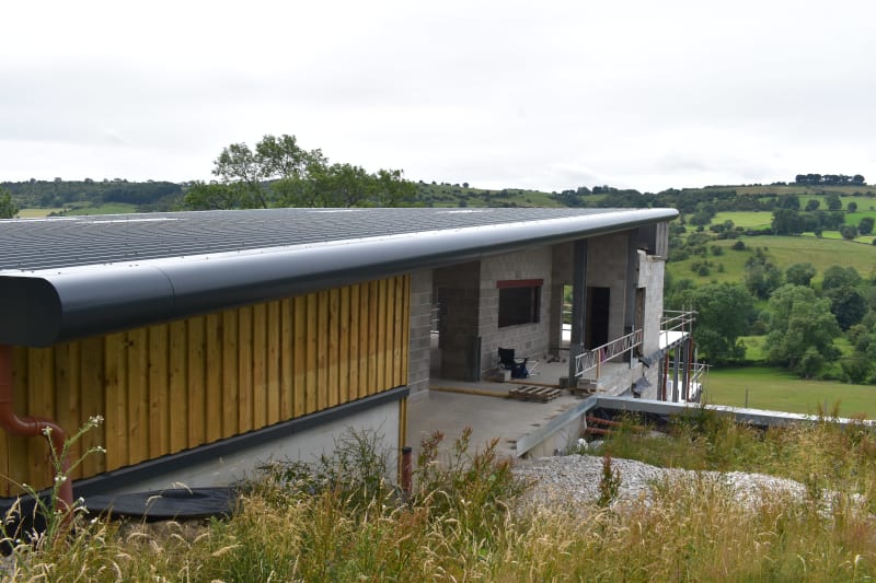 Modern rural building under construction with timber cladding, curved metal roof, and concrete block walls in countryside setting