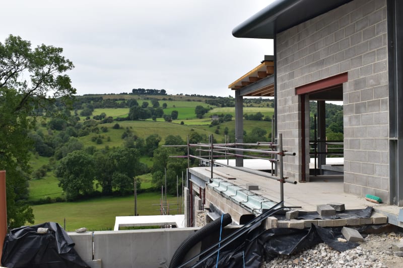 Modern residential building under construction with concrete block walls and steel framing overlooking lush Irish countryside