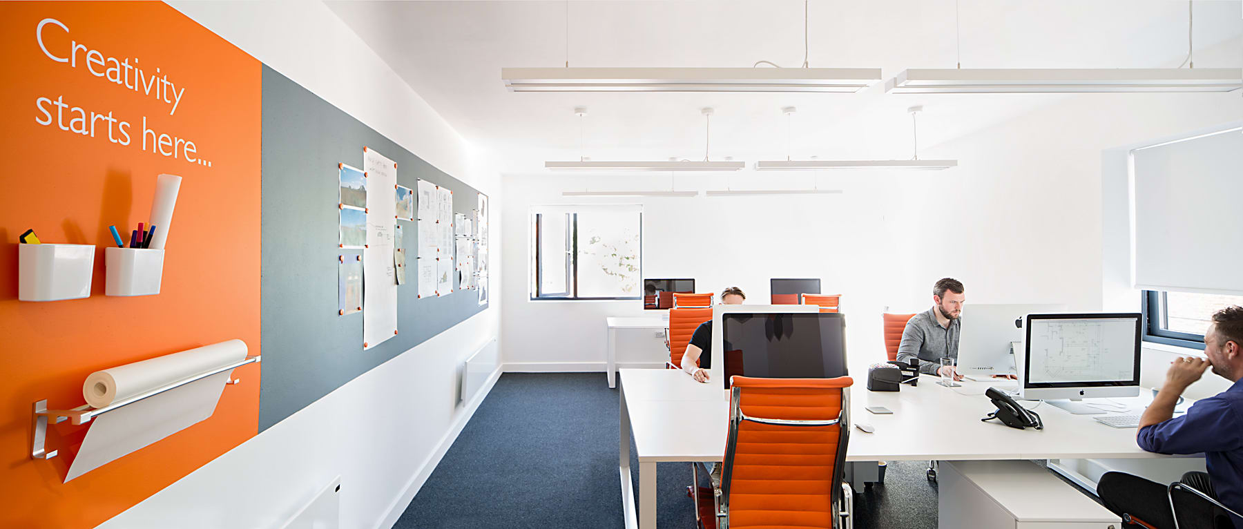 Open-plan design studio with orange accent wall and staff working at desks with orange task chairs
