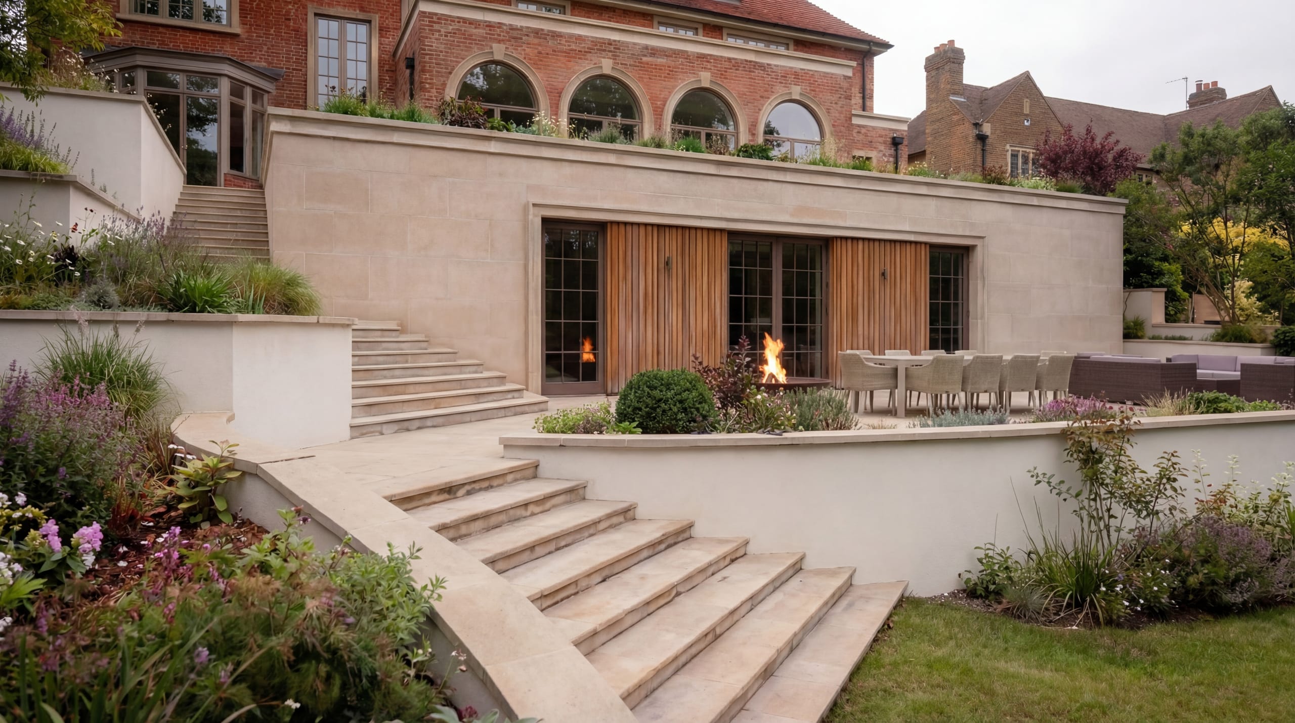 Modern limestone garden extension with timber shutters, outdoor dining terrace, fire feature, and tiered landscaped gardens