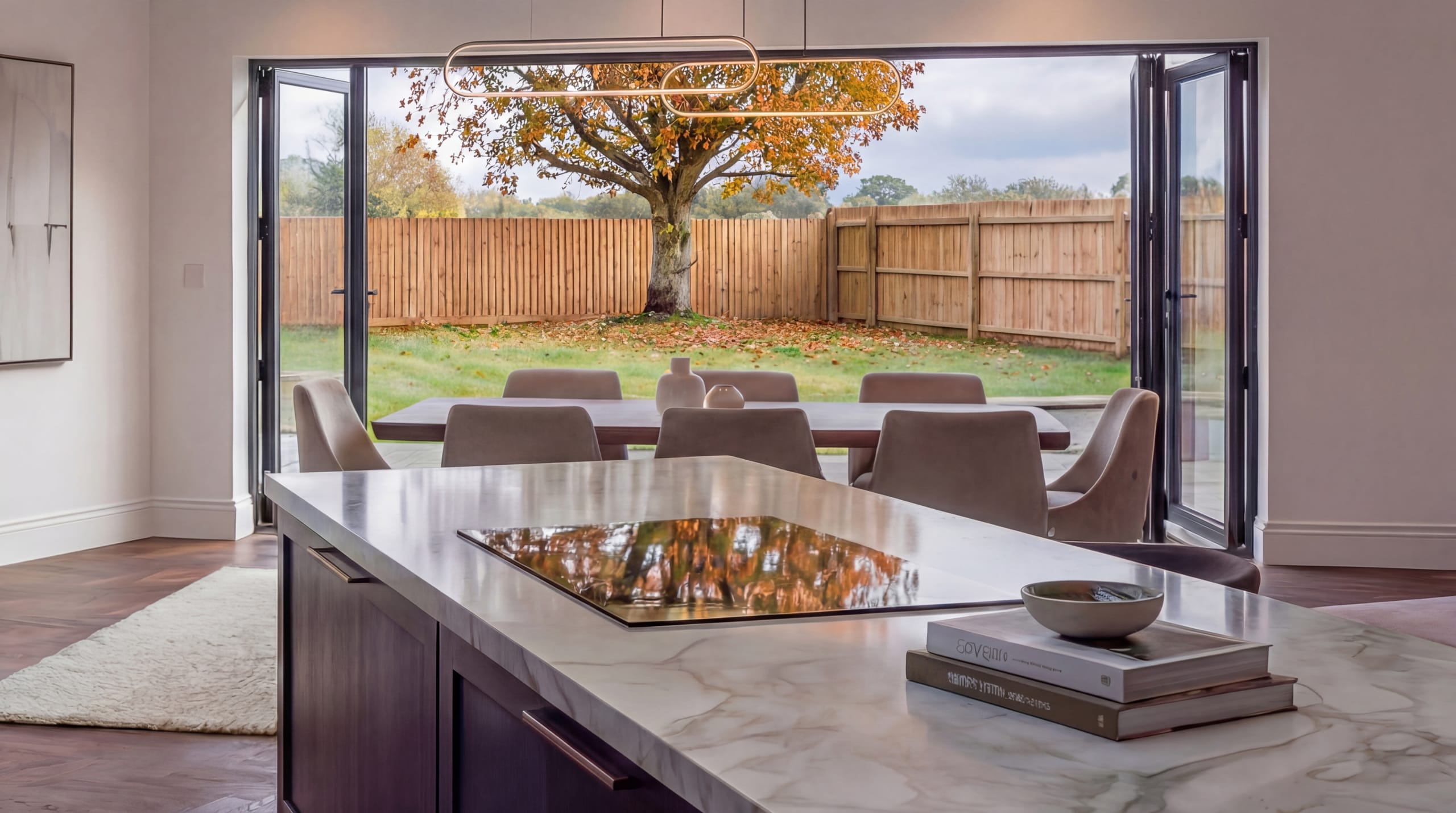 Visualisation looking across the kitchen island and dining table through bifold doors to the garden