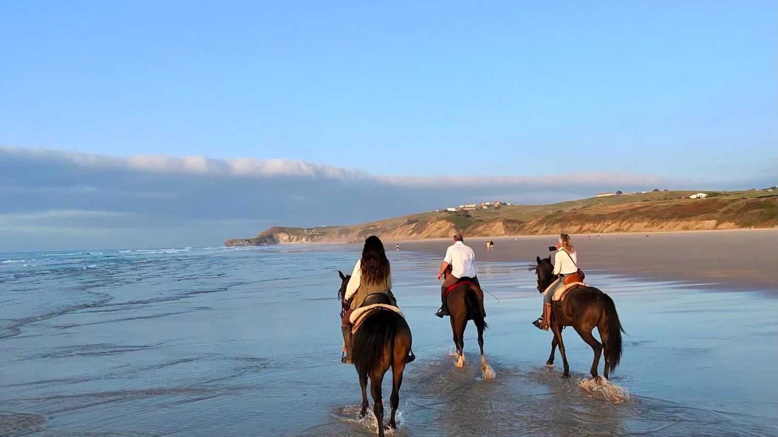 Grupo de jinetes cabalgando por la orilla del mar