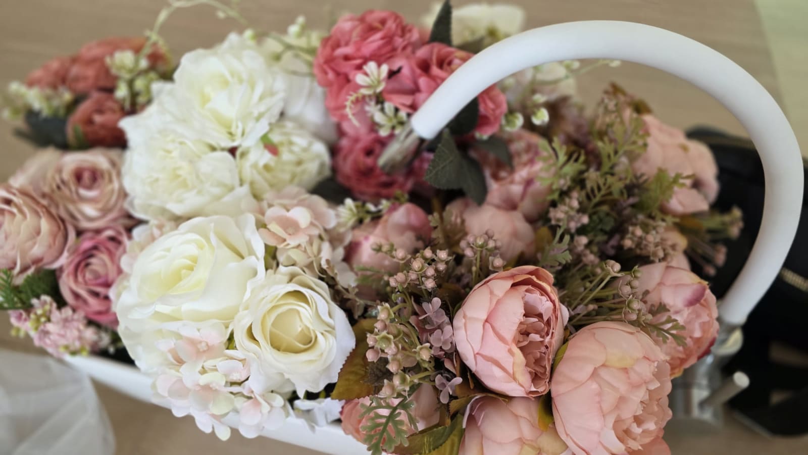 Cesta blanca llena de peonías, rosas y flores en tonos rosa y crema