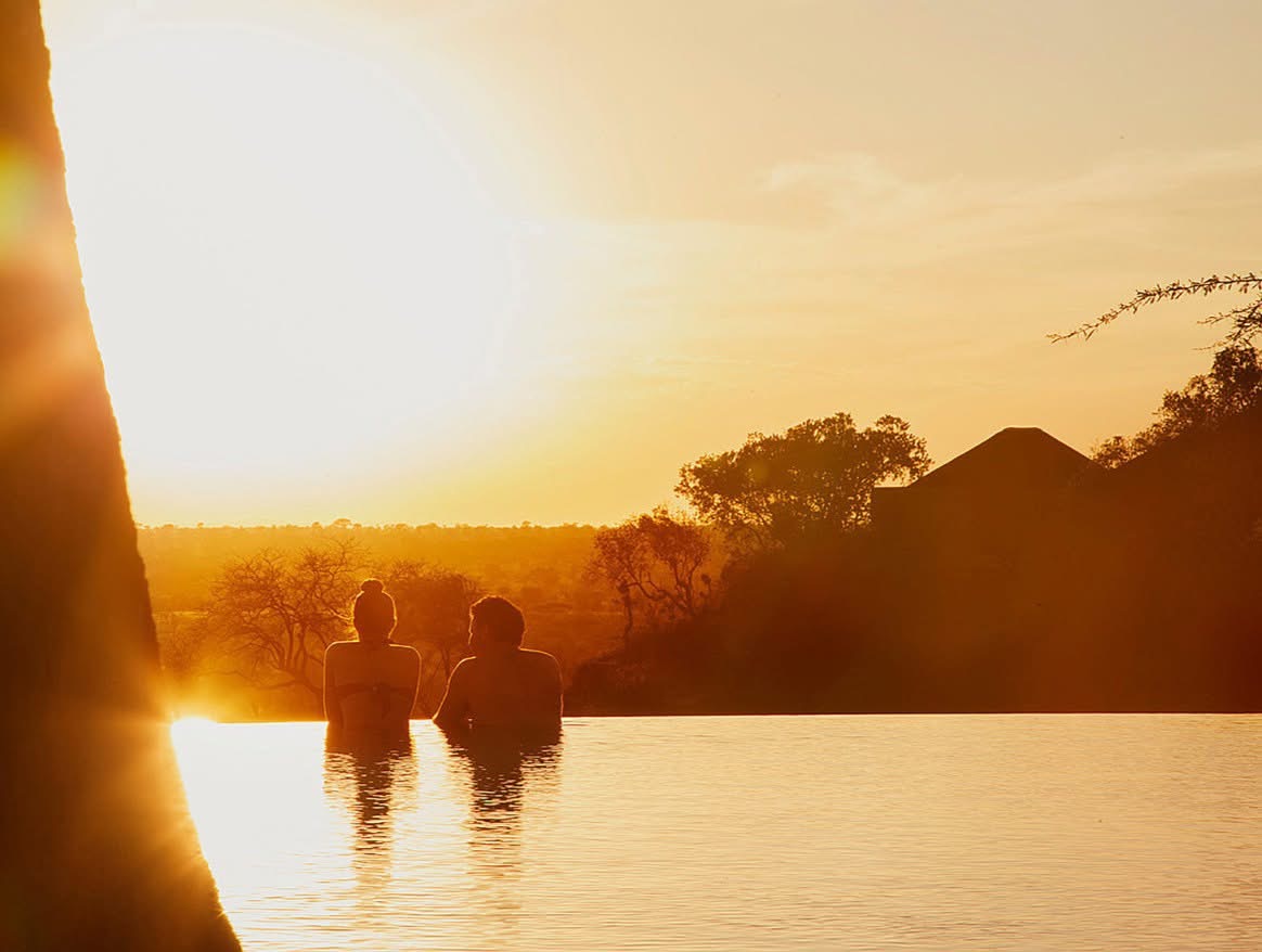 Couple watching sunset from a private lodge deck overlooking the Serengeti plains, Tanzania honeymoon safari