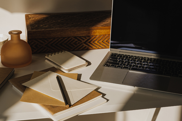Laptop, notebook, pen, and envelopes arranged on a sunlit desk, representing a calm hormone optimization consultation.