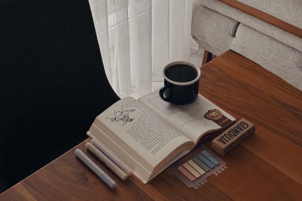 Open book, coffee, and writing supplies on a wooden table, representing a calm wellness routine and thoughtful peptide support.