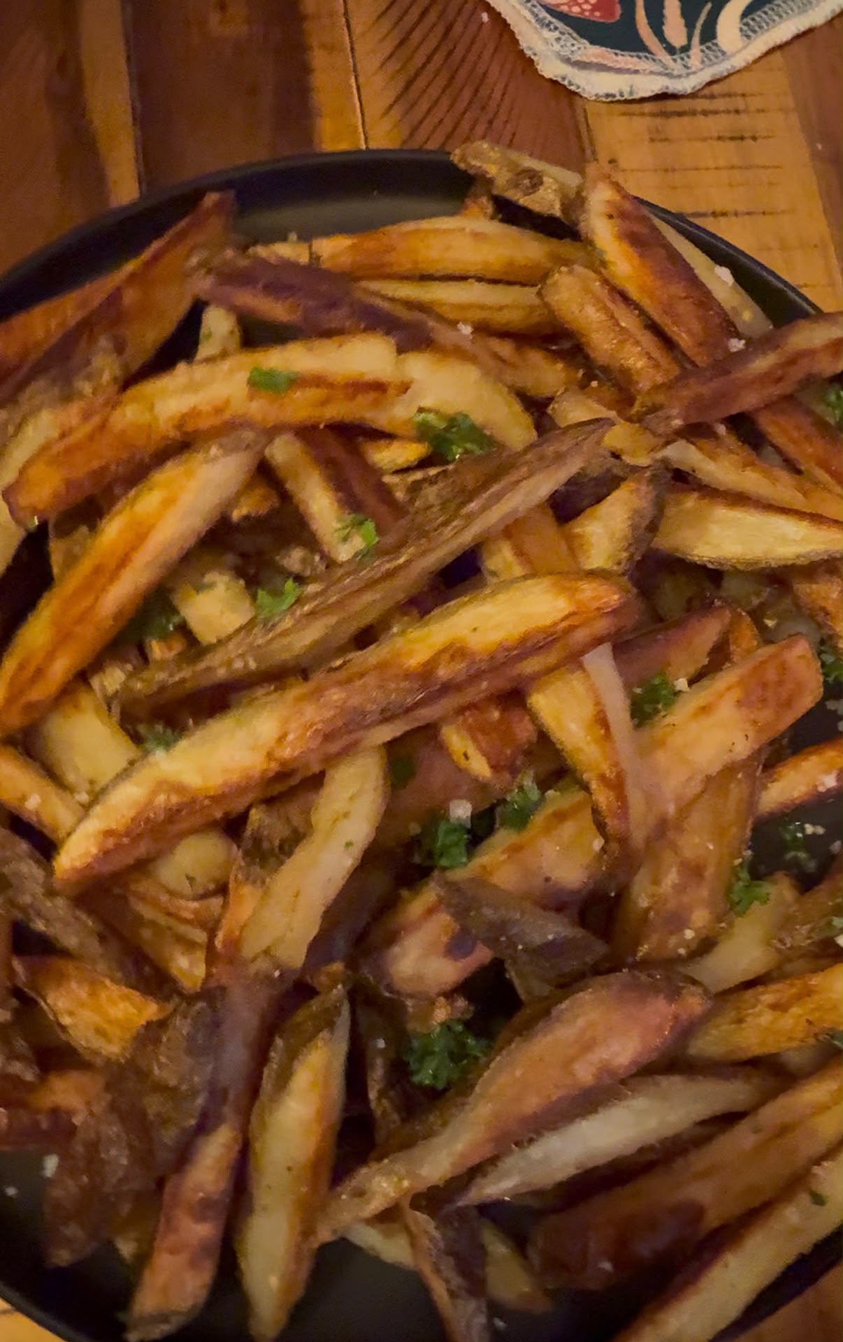 Golden crispy homemade fries tossed with fresh herbs and flaky salt in a black serving bowl.